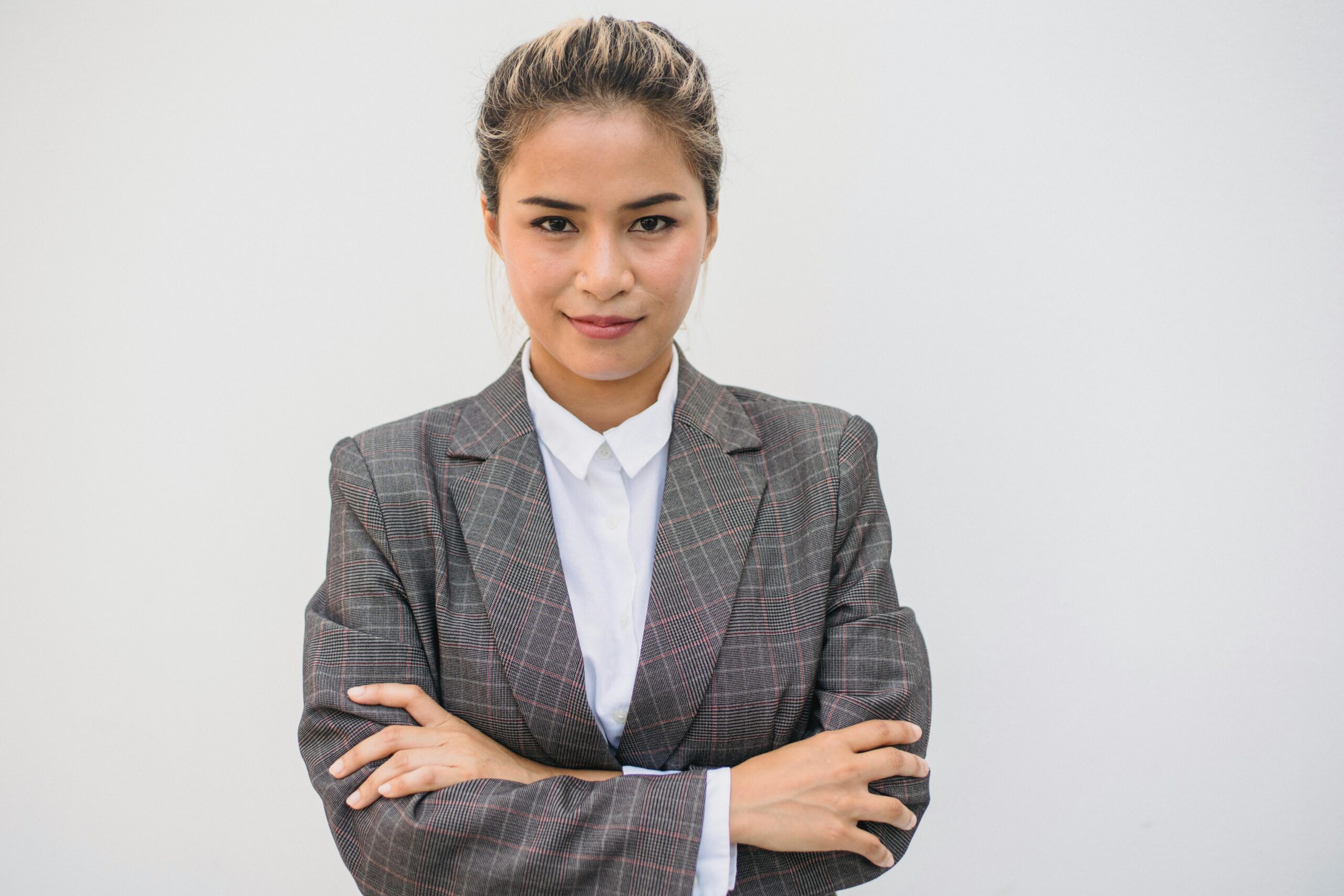 Portrait of a confident Asian woman in a plaid blazer with arms crossed, smiling and posing.